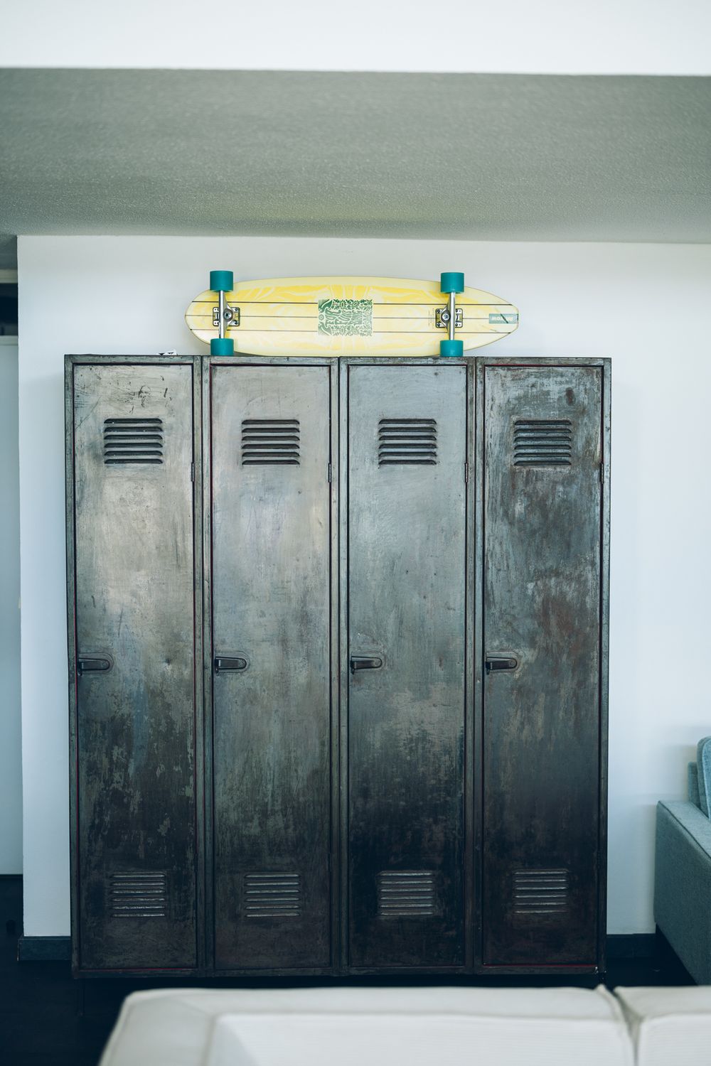 A row of vintage metal lockers with a yellow skateboard balanced on top against a white wall.