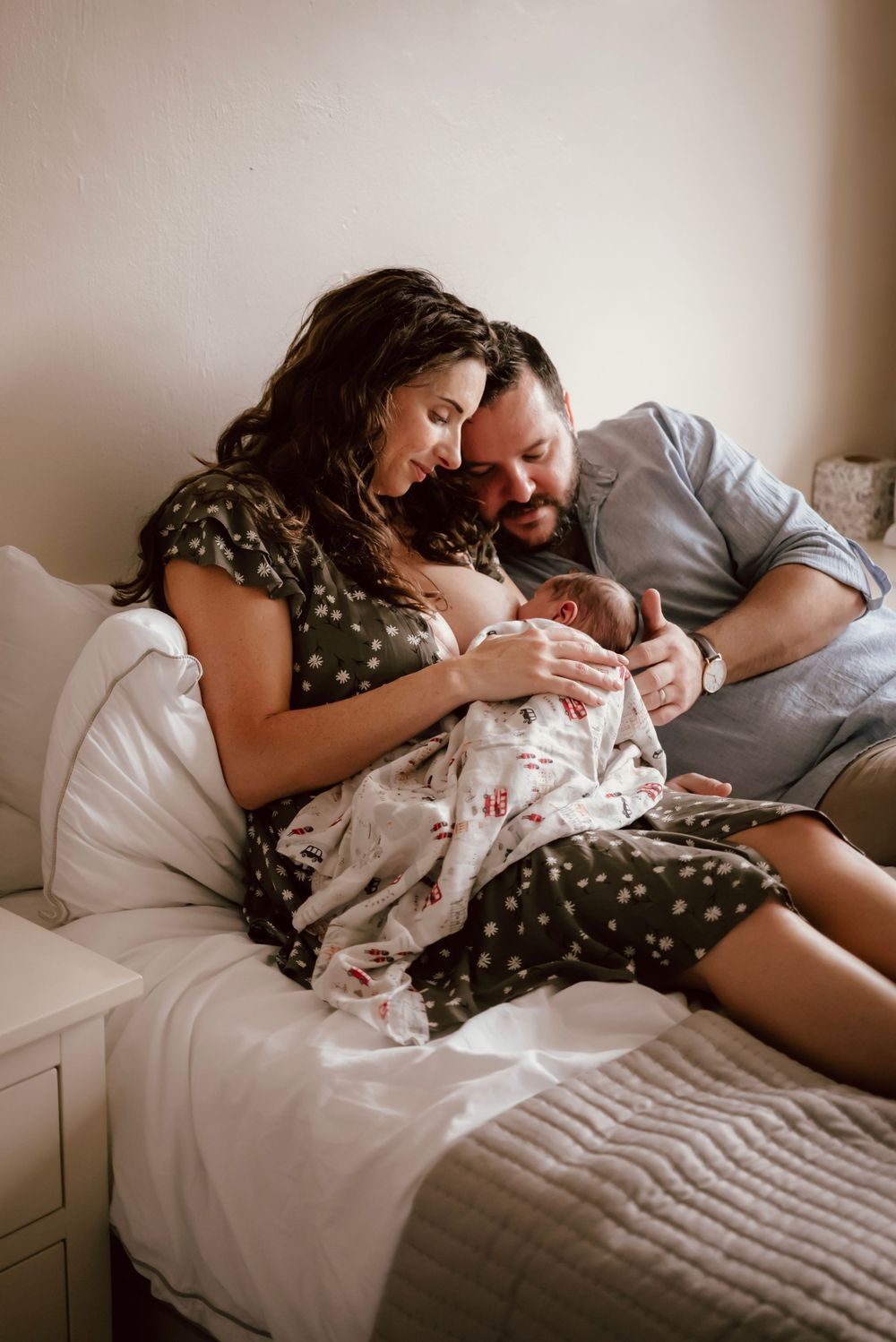 A loving couple cuddle as the mother breastfeeds her newborn baby while relaxing on a cozy bed at home.