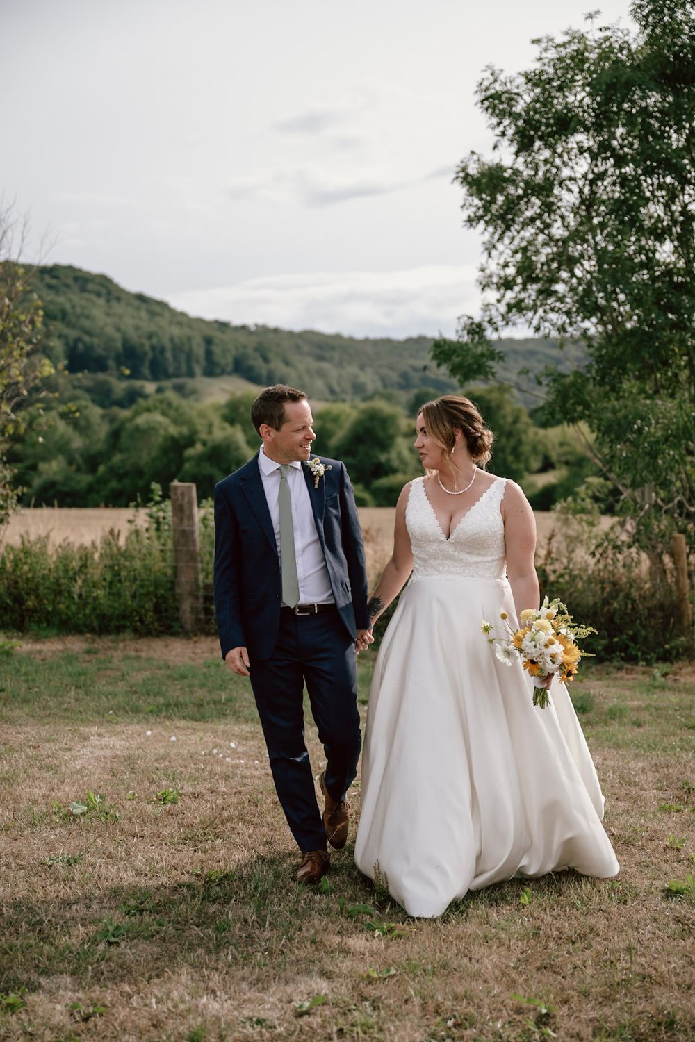 A couple walks together and shares intimate moments in a scenic rustic outdoor setting with rolling hills in the background.