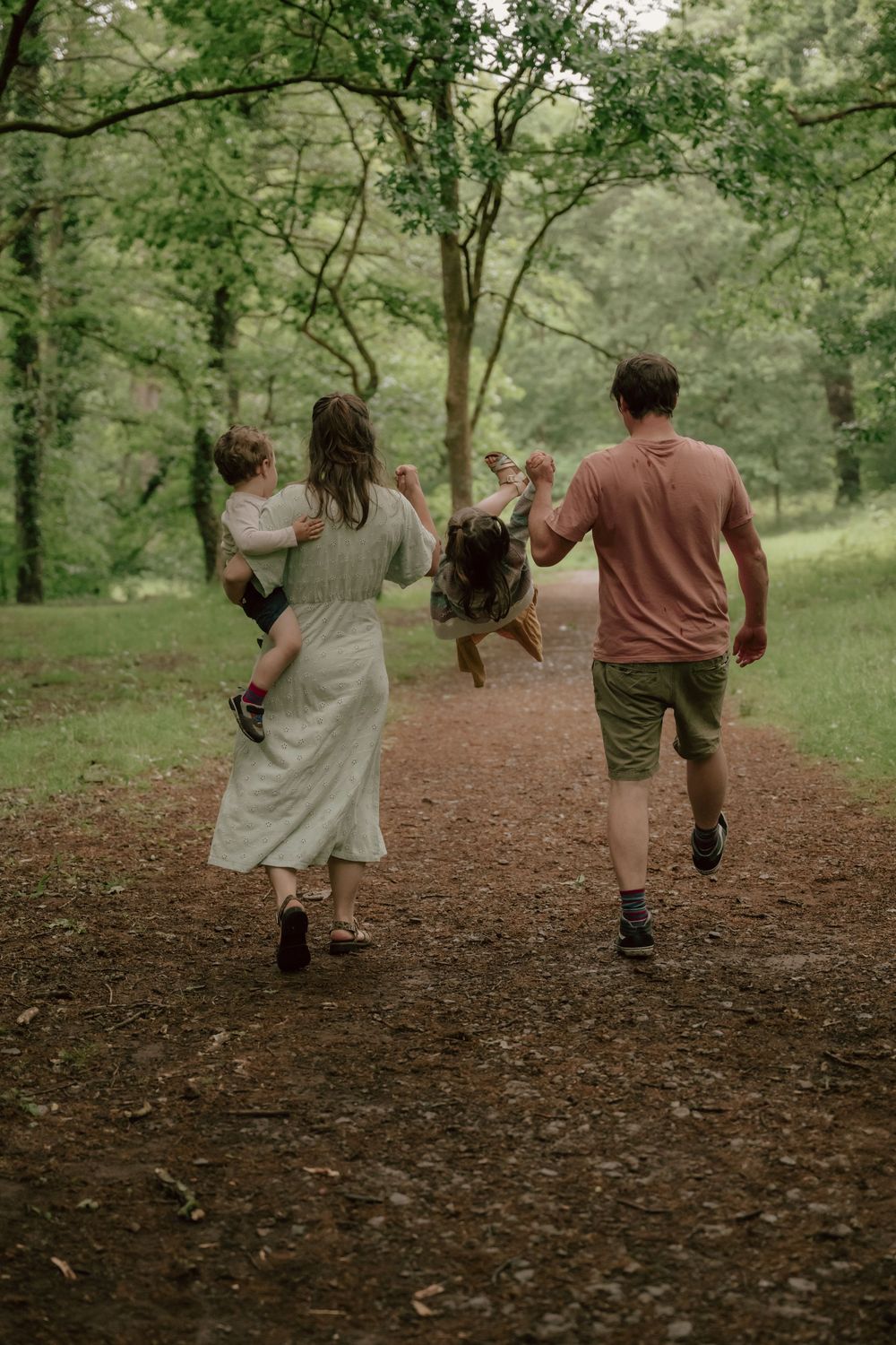 Family enjoying a walk together on a wooded trail surrounded by lush green trees on a peaceful afternoon.