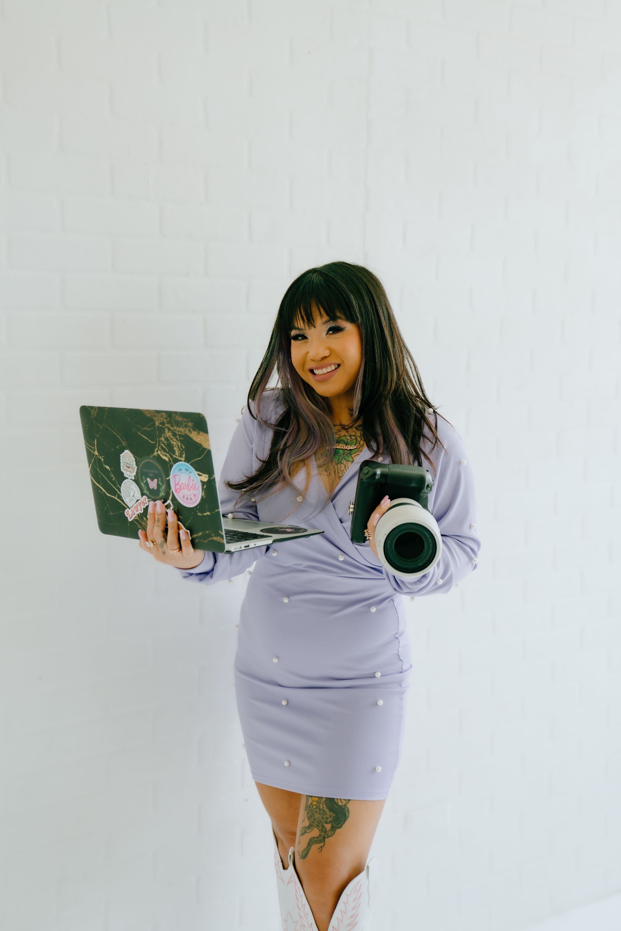 Lifestyle portrait with laptop and camera against white wall in purple dress outfit.