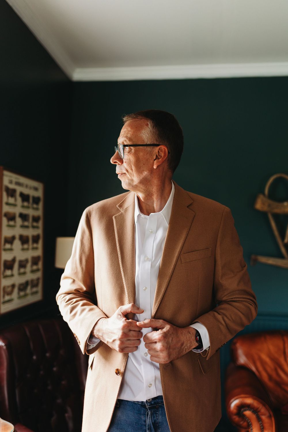 Groom in tan blazer and glasses buttoning jacket in elegant dark-walled room at Full Bloom Farmhouse in Abingdon, VA