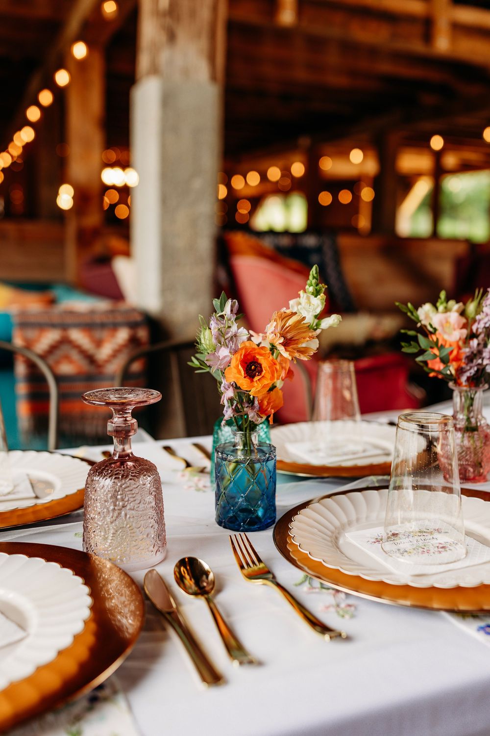 An elegant wedding reception table set with gold flatware, pink glassware, and colorful floral centerpieces at Full Bloom Farmhouse.