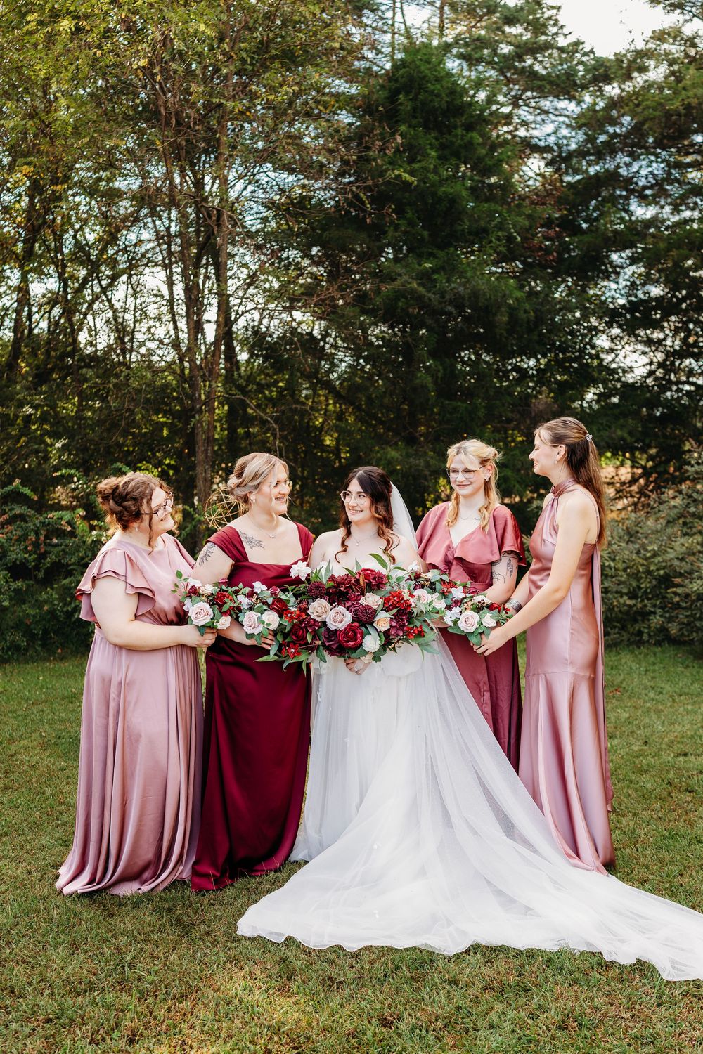 Bride with four bridesmaids in pink and burgundy gowns holding bouquets outdoors in garden setting at Wildflower Farm in Greenville, TN.