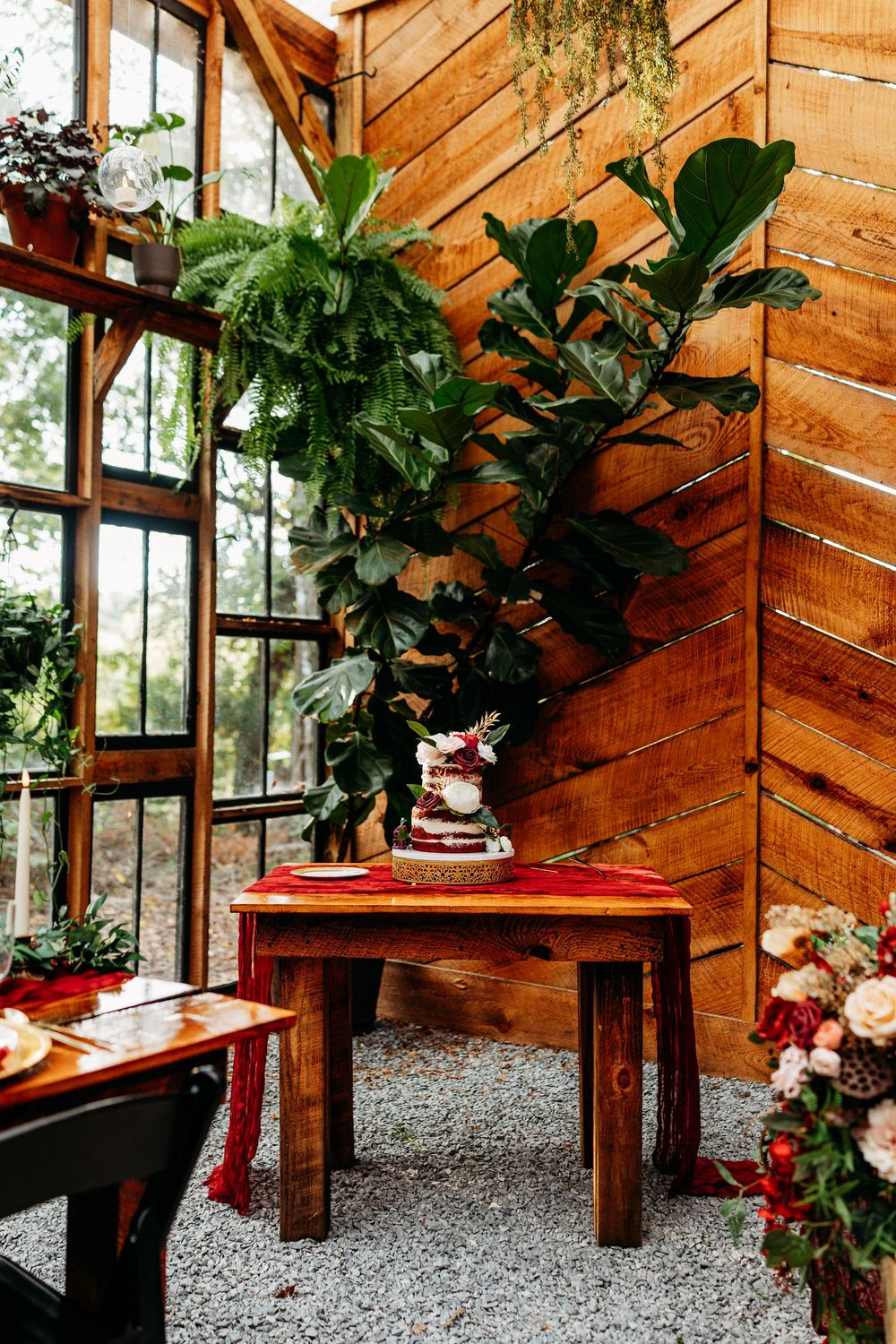 Rustic wedding cake display on wooden table beside large fiddle leaf fig tree at Wildflower Farm in Greenville, TN.