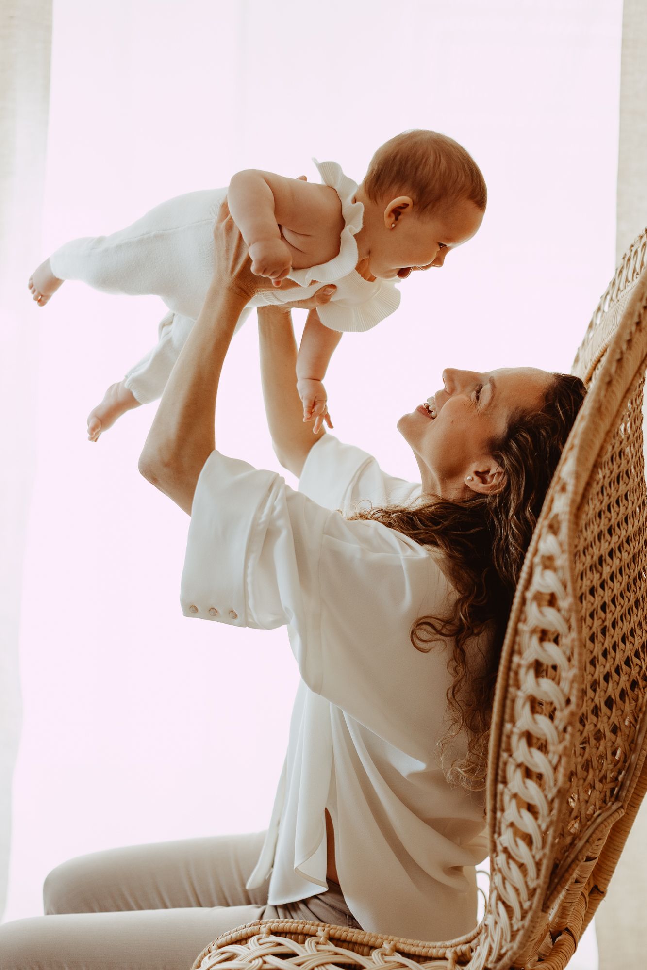 Parent and baby sharing playful moment in wicker chair.
