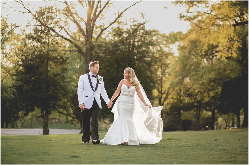A romantic wedding couple poses in a sun-dappled park setting during golden hour.
