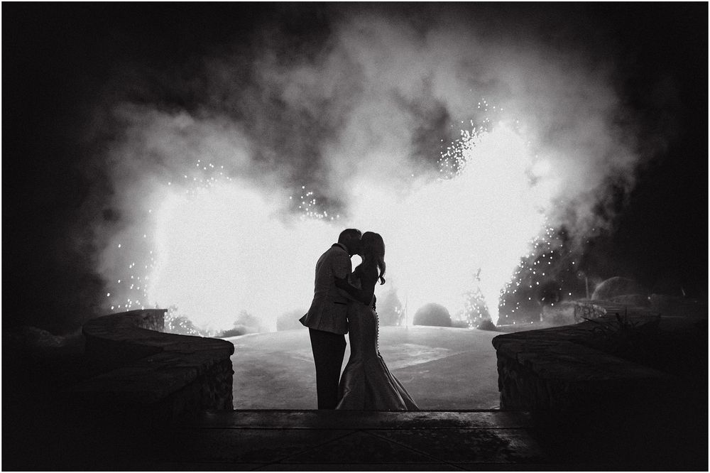 Silhouettes of a couple embrace against a dramatic backlit sky creating a romantic monochrome scene.