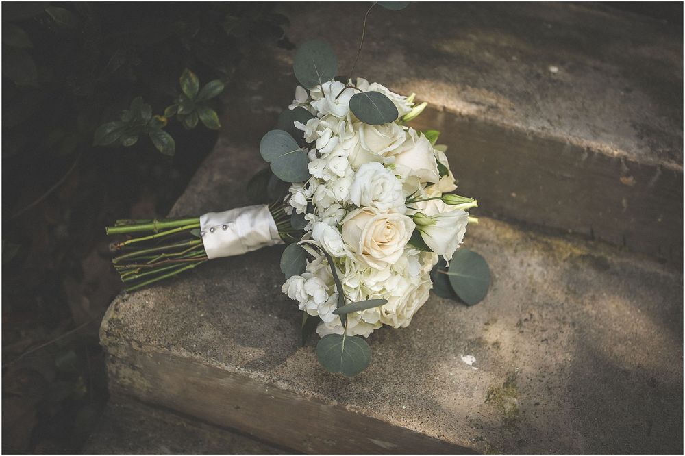 White and cream floral bouquet with eucalyptus leaves rests on a rustic wooden surface in natural lighting.