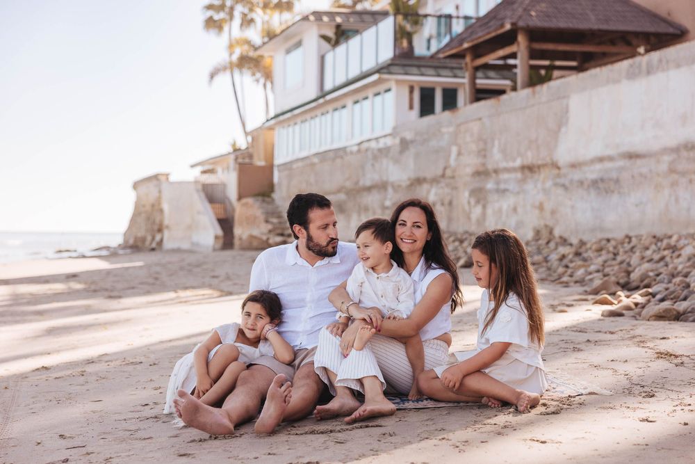Family lifestyle photography session at beach with palm trees and buildings visible.