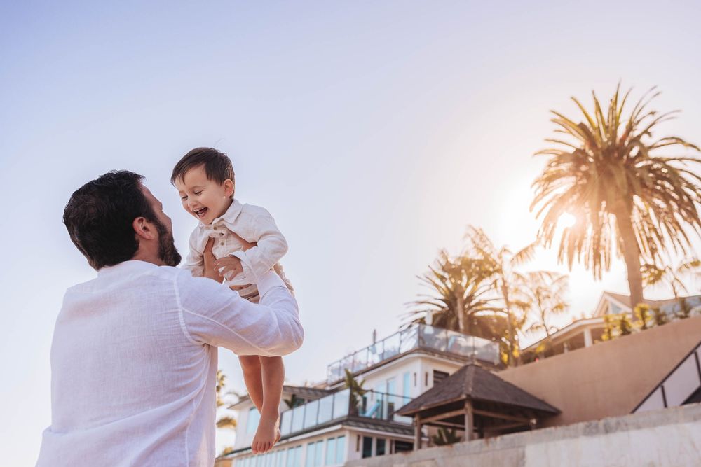Sunset beach family photoshoot with palm trees silhouetted against bright sky.