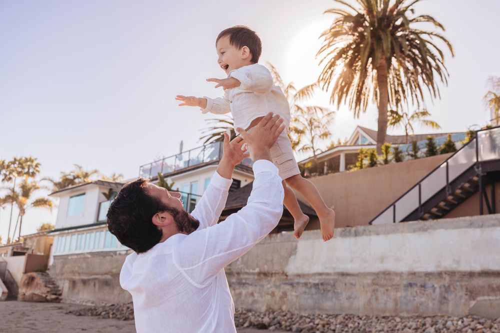 A joyful moment at sunset with palm trees and coastal architecture in the background.