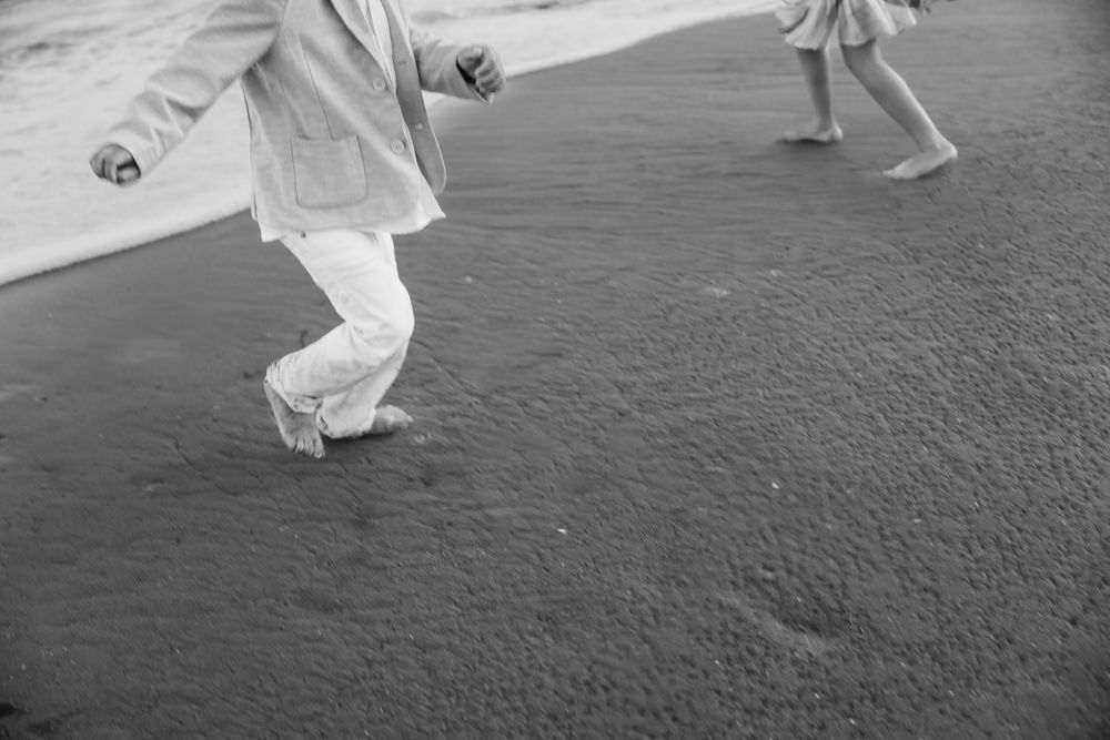 Black and white image of feet in flowing white clothing dancing or moving on a dark surface.