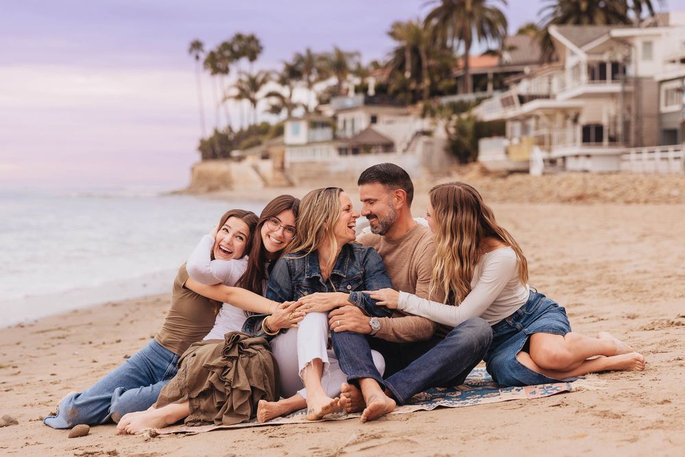 A family wearing matching denim outfits relaxes together on a sandy beach at sunset.