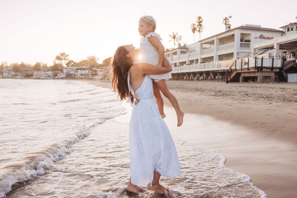Family enjoying a sunset beach photoshoot in white outfits along the shoreline.