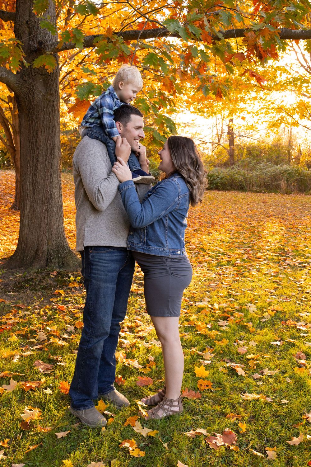 A family shares a tender moment among vibrant autumn foliage as golden sunlight filters through the trees.