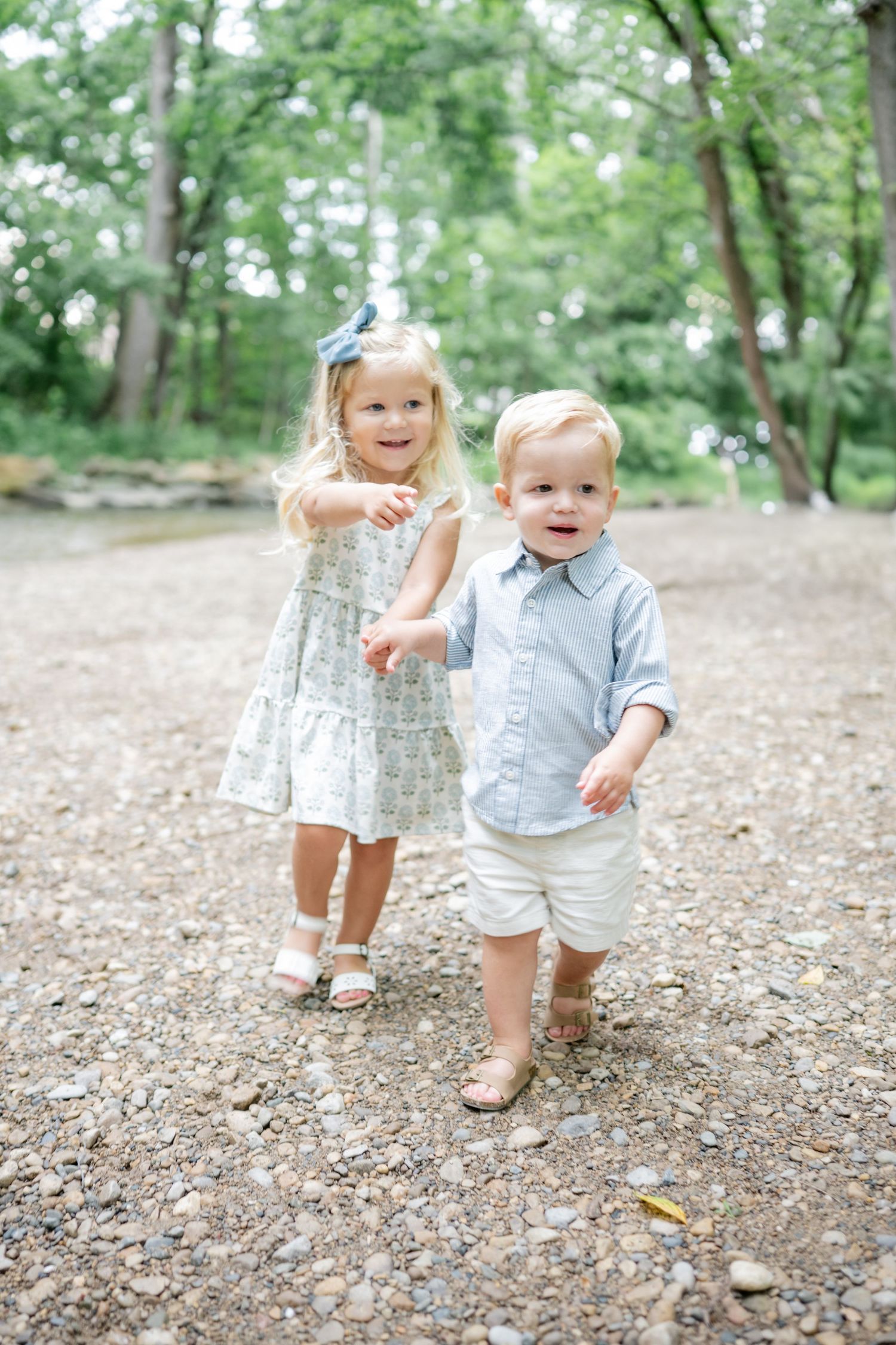 mama holds her twins in her arms while smiling lovingly down at them.  in wooded area of park in carmel indiana