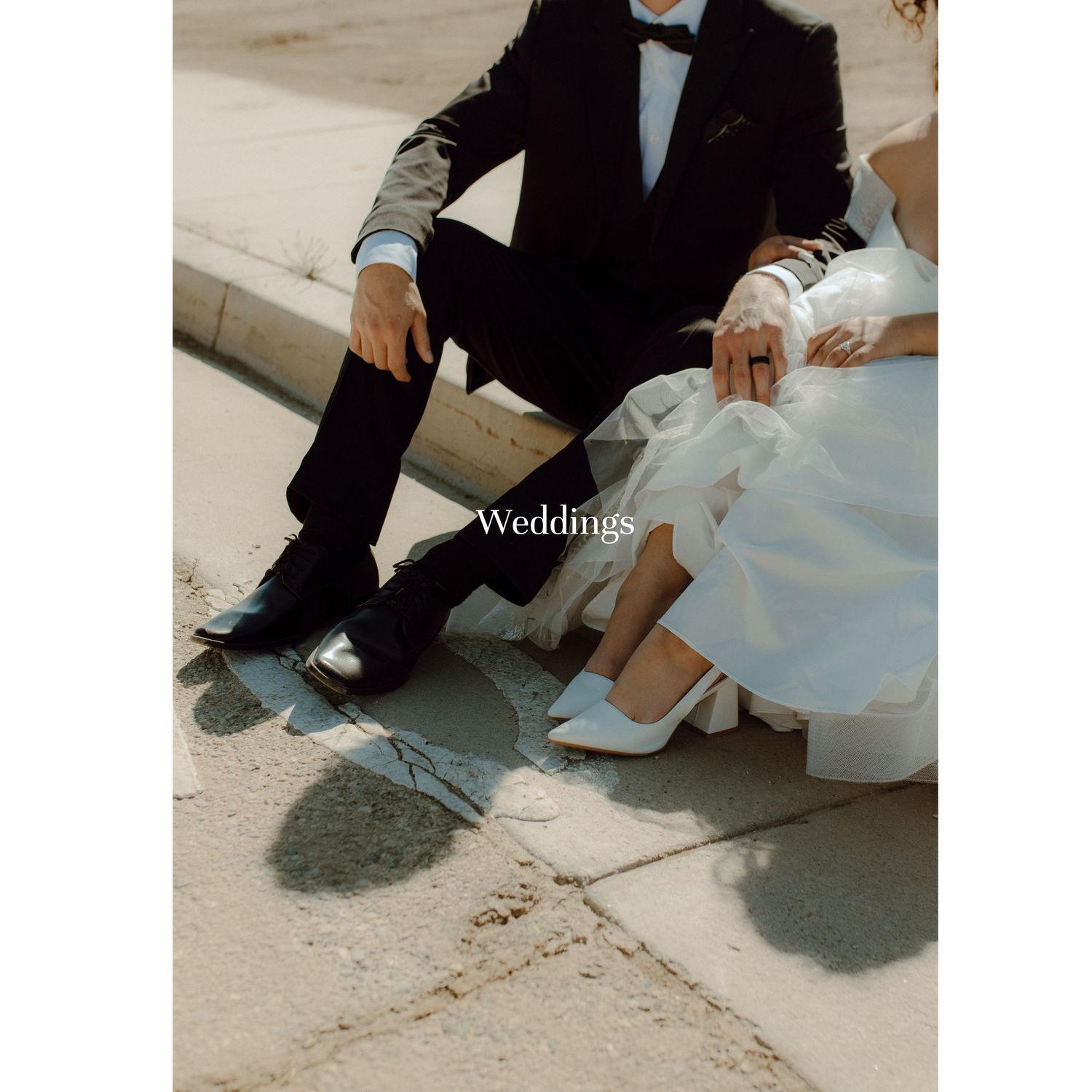 Close-up view of a groom in black tuxedo and bride in white dress sitting together showing their elegant wedding shoes.
