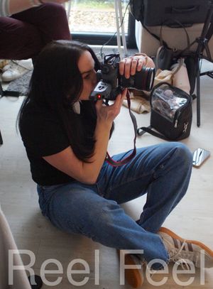 Photographer in black shirt and jeans crouches down while taking photos with a professional camera.