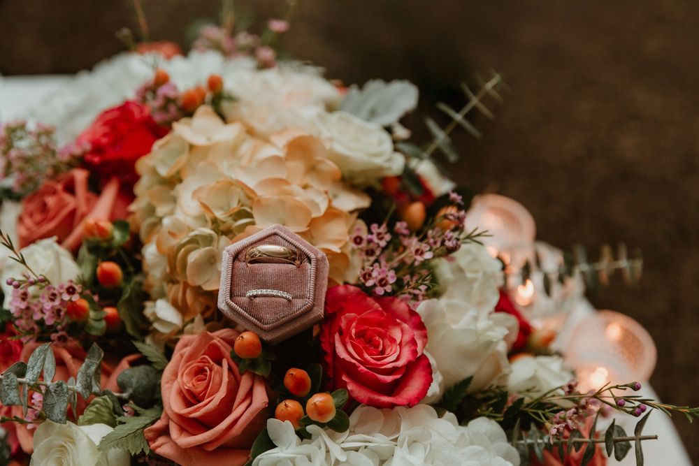 Elegant wedding ring box nestled among red roses, hydrangeas, and greenery in a bridal bouquet.