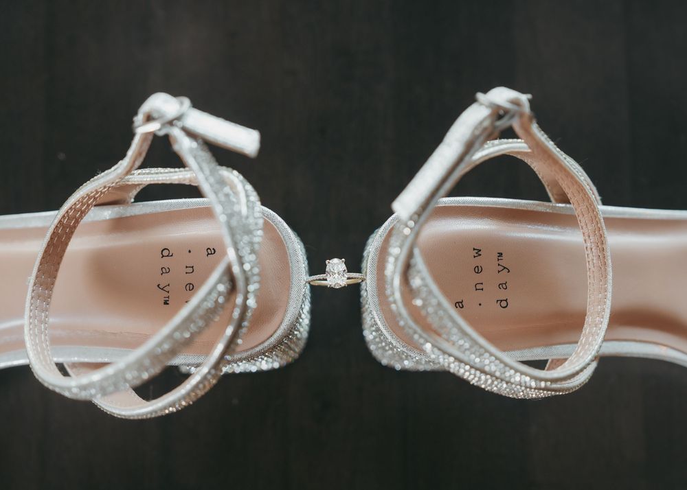 Sparkling crystal-embellished silver strappy wedding heels displayed back to back on a dark wooden surface.