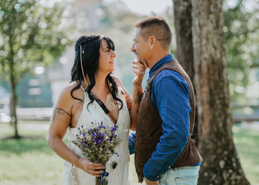 Bride with wildflower bouquet laughing with groom in brown vest outdoors.