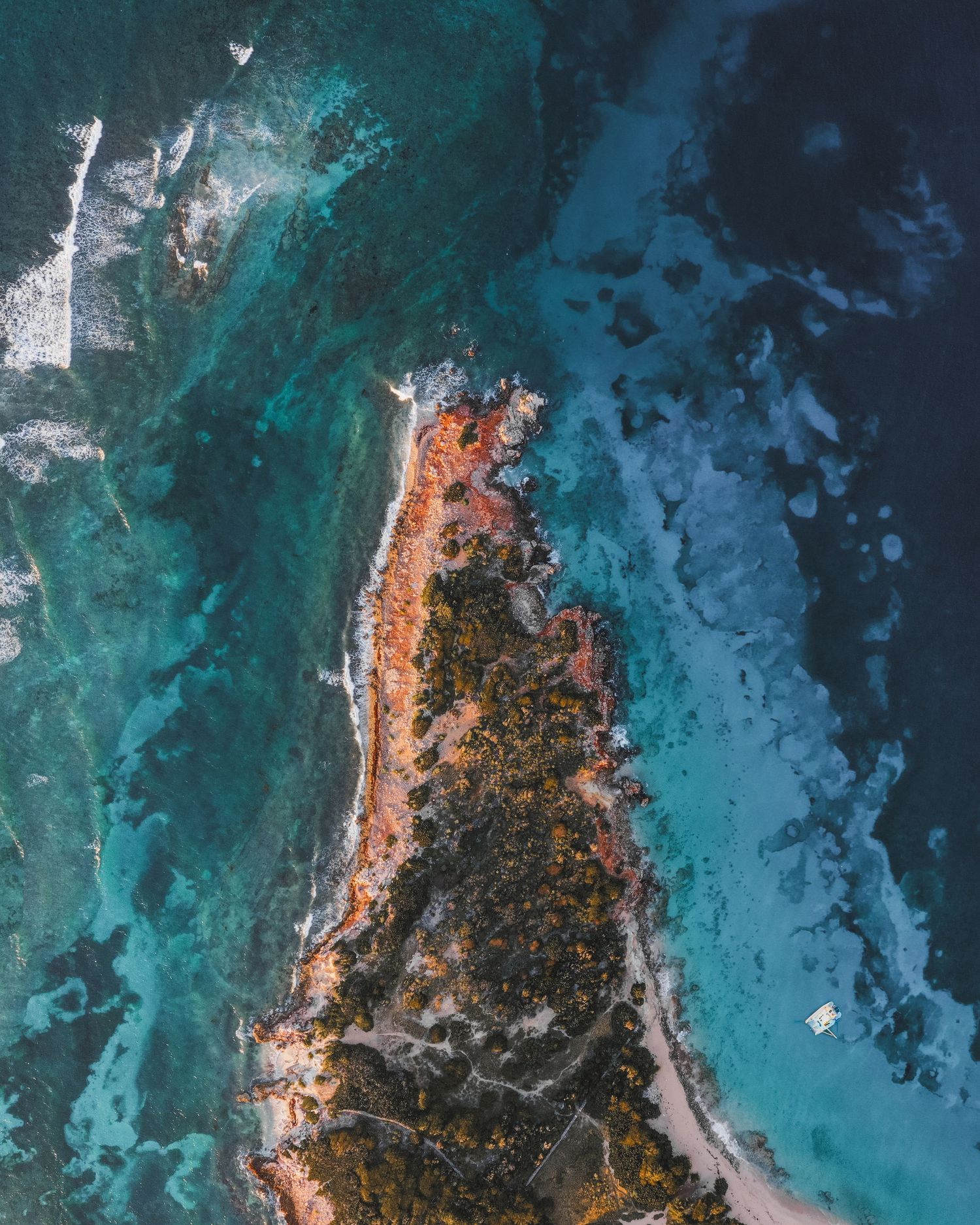 Aerial view of a rugged coastline with turquoise waters meeting red cliffs and rocky shores along ocean edge.