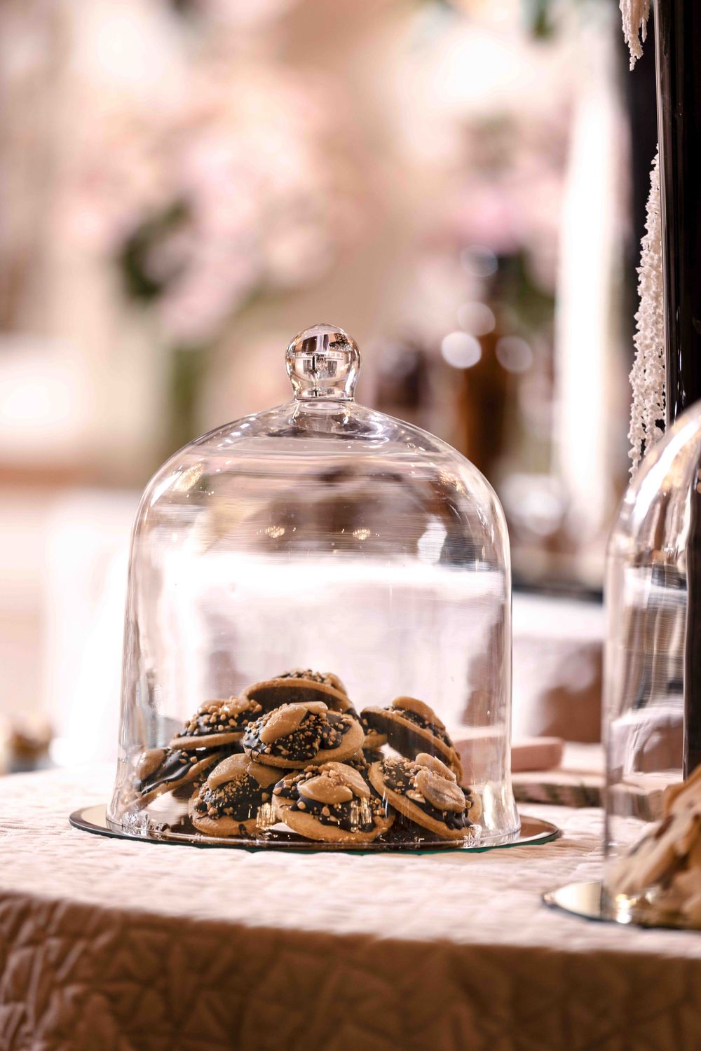 Cookies displayed under a clear glass cloche dome on textured tablecloth.
