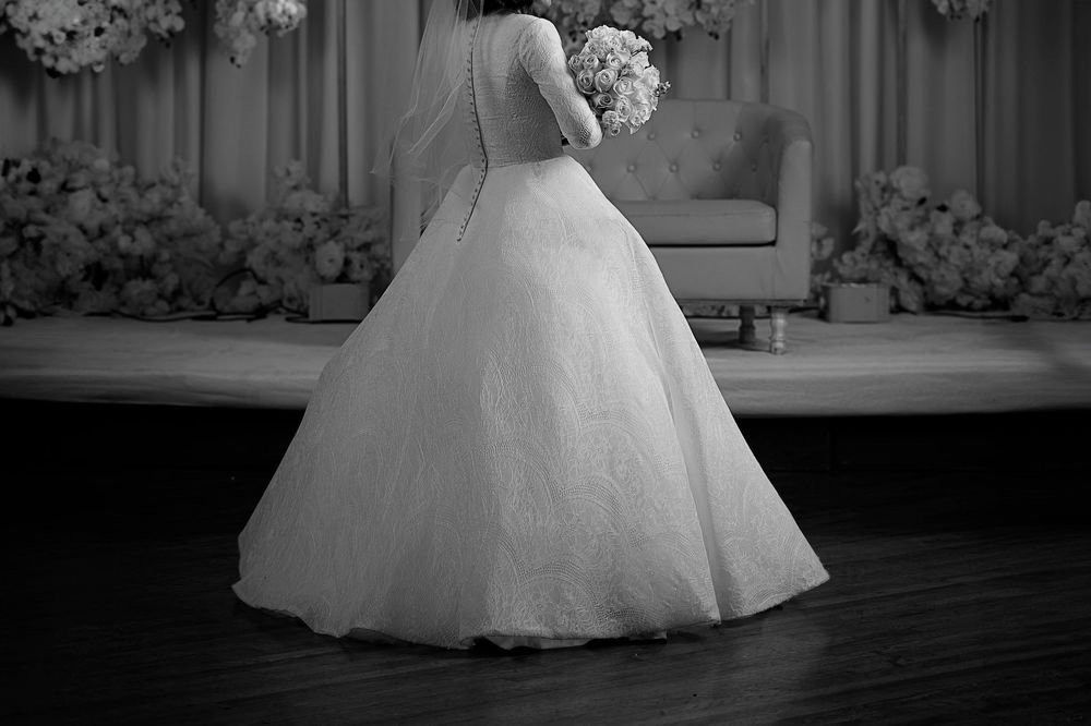 A flowing white wedding dress twirls gracefully on a dark wooden dance floor during a reception.