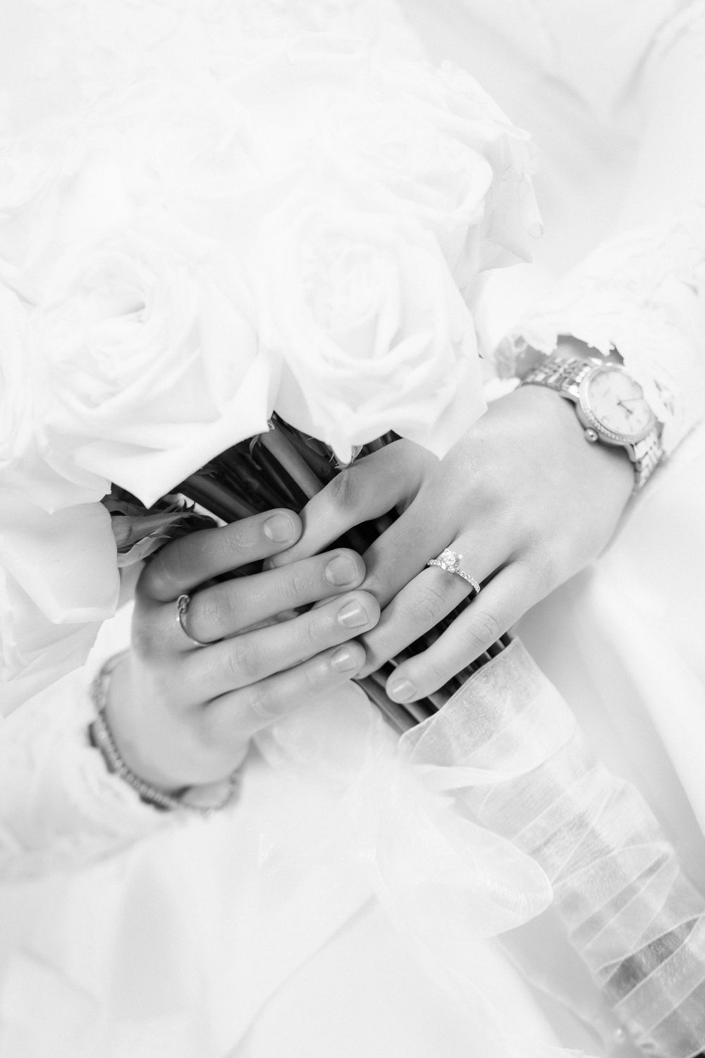 Black and white photo of bride and groom hands with wedding rings and bouquet of white roses.