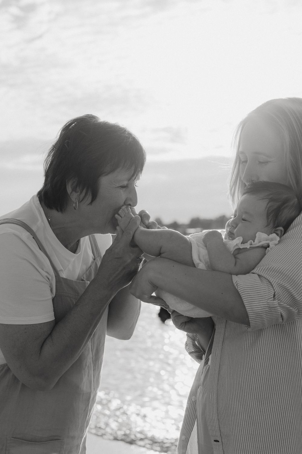 A tender black and white family moment captured at the beach as an infant is held by two adults.