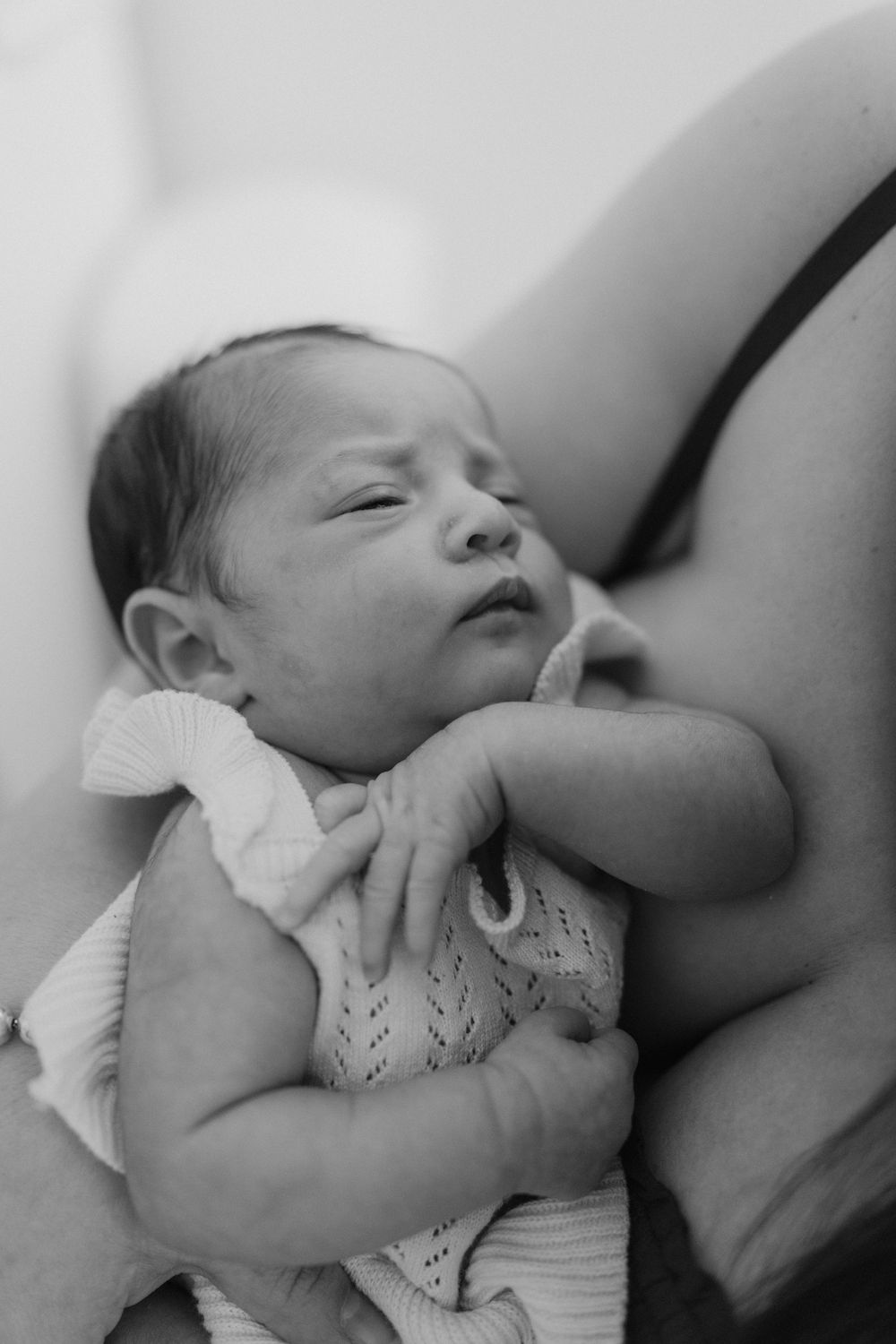 A sleeping newborn baby wearing a knitted white outfit rests peacefully in black and white photography.