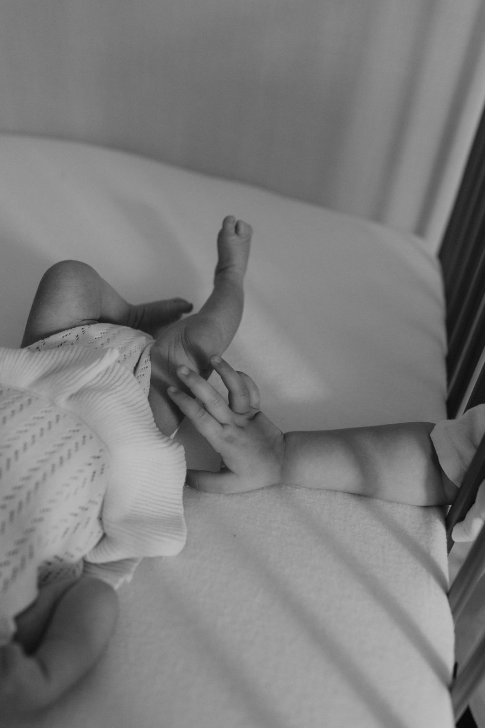 Small hand wearing a white knitted glove rests on a light bedsheet in a monochrome photograph.