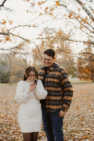 A couple laughing together on an autumn day surrounded by fallen leaves.