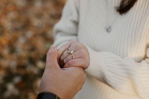 Close-up shot of hands holding while showing off an engagement ring against a cream sweater.