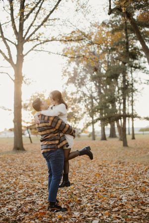 A joyful couple sharing a romantic moment among fallen autumn leaves at sunset.