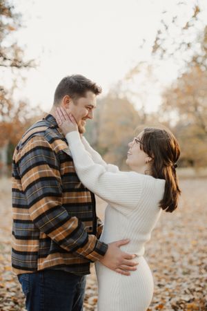 A couple sharing an intimate moment while standing in a park covered with autumn leaves.
