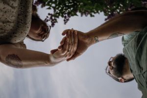 Two hands reaching to hold each other against a bright sky background.