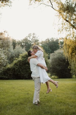 A romantic couple embraces in a sunlit garden with trees in the background during golden hour.