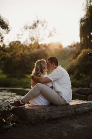 A couple shares an intimate moment by the water during sunset while sitting on a log.