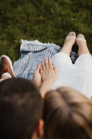 Overhead view of a couple sitting close together on grass showing their feet.