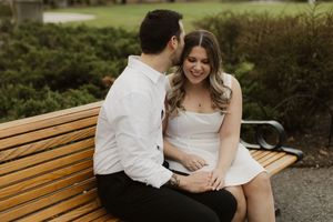 A couple shares a joyful moment together while sitting on a wooden bench in a garden setting.