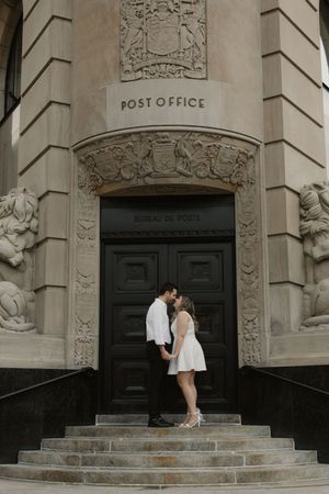 A romantic couple stands on the stone steps of a historic post office building with ornate architectural details.