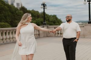 A couple stands together in white and black formal attire during an outdoor photo session on a stone bridge.