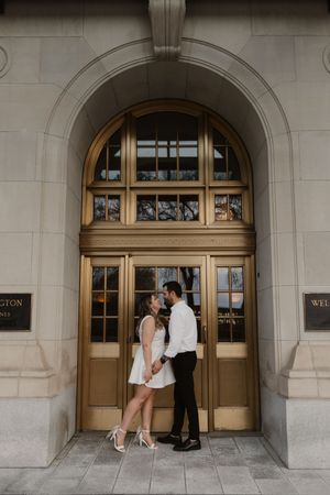 A couple share an intimate moment in front of three elegant arched doorways of a historic stone building.