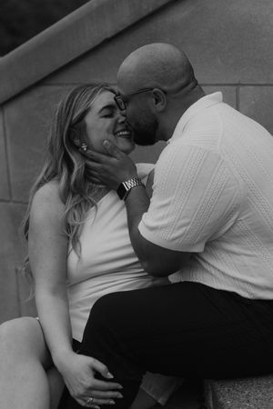 A romantic black and white photo of a couple sharing an intimate moment while sitting together outdoors.