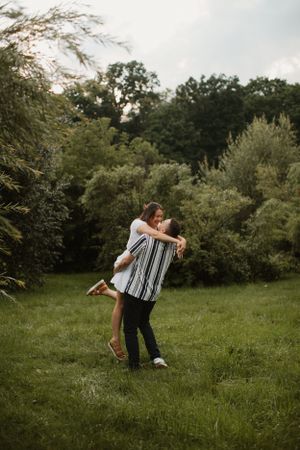 A joyful couple embraces and spins in a green garden setting during golden hour.
