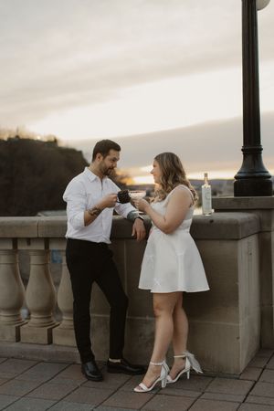 A couple in formal attire shares romantic moments on a stone balcony at sunset.
