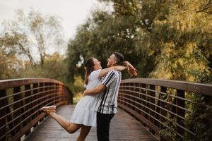 A romantic embrace on a wooden bridge surrounded by autumn trees.