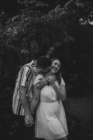 An intimate black and white portrait of a couple sharing a tender moment outdoors.